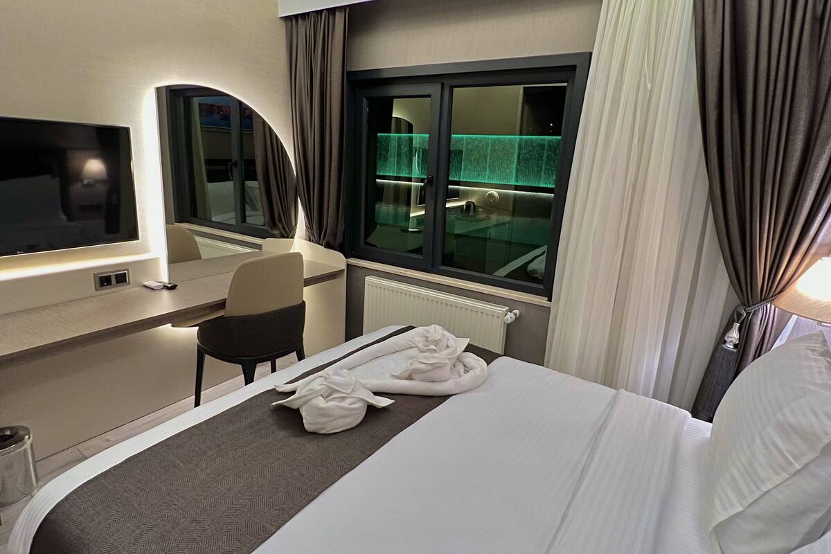 Une chambre d’hôtel avec un lit, un bureau, une chaise, une télévision et une fenêtre avec des rideaux.