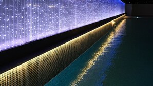 Una piscina amb una paret il·luminada i un paviment de rajoles.