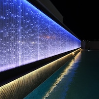 Una piscina con una pared iluminada y suelo de baldosas.
