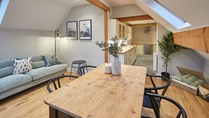 A modern living room with a wooden dining table, a light blue sofa, and a small black chair. There are two framed pictures on the wall, a floor lamp, and a potted plant. - Host & Stay | Sleepers @ No.8 (Pickering)