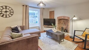 A living room with a sofa, a coffee table, a TV, a fireplace, and a window with curtains. - Host & Stay | Sleepers @ No.8 (Pickering)