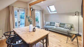 A cozy living room with a wooden dining table, a sofa, and a skylight. - Host & Stay | Sleepers @ No.8 (Pickering)