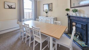 A dining room with a wooden table and white chairs, a fireplace, and a map on the wall.