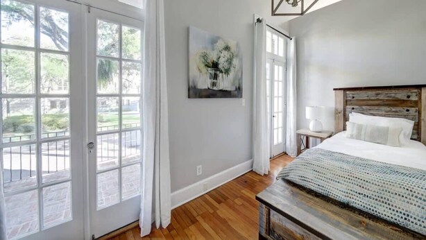 Une chambre à coucher avec un lit, une table de chevet, une lampe, un tableau et une vue sur l’extérieur grâce à de grandes fenêtres.