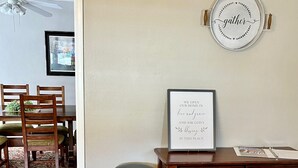 A living room with a brown leather couch, a framed inspirational quote on the wall, a round mirror with the word "gather" on it, and a dining area in the background. - The Spacious, Vintage House on the Ranch
 (Enoch)