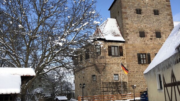 Een historisch stenen gebouw met een toren, sneeuw bedekte bomen en een heldere blauwe lucht.