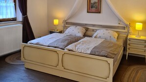 Een bed met hemelbed, twee nachtkastjes met lampen, een schilderij aan de muur, en een raam met gordijnen.