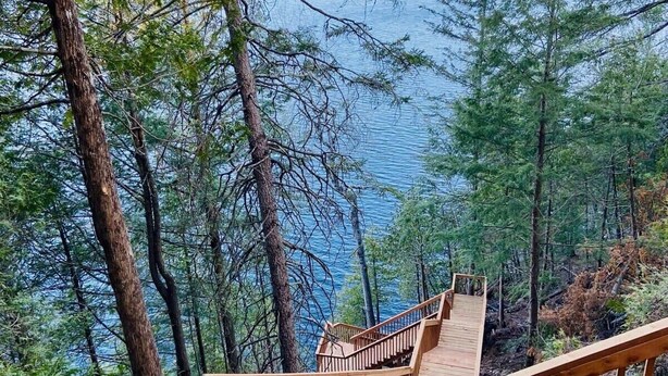 Un escalier en bois mène à une plateforme d’où l’on peut admirer un lac entouré d’arbres.
