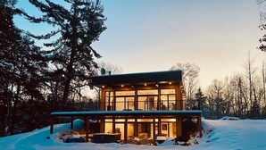 Une maison moderne à deux étages, dotée d’une façade en verre, entourée de neige.