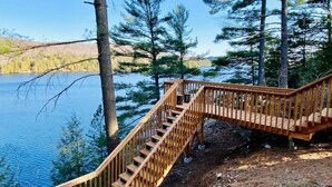 Un escalier en bois mène à une terrasse en bois surplombant un lac entouré d’arbres.