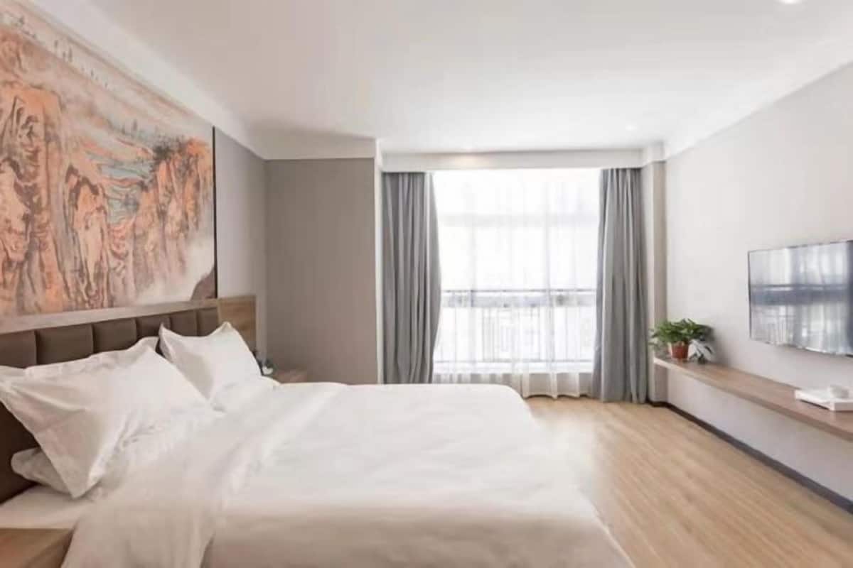 Una habitación de hotel moderna con una cama grande, un cuadro en la pared, una ventana con cortinas y un televisor montado.