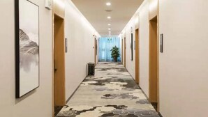 Un pasillo de hotel con alfombra estampada, puertas de madera y cuadros en las paredes.