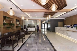 Um saguão de hotel com um balcão de recepção, uma longa mesa de jantar e uma escadaria.