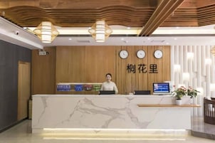 A hotel reception desk with a wooden panel wall, a clock, and a digital screen.