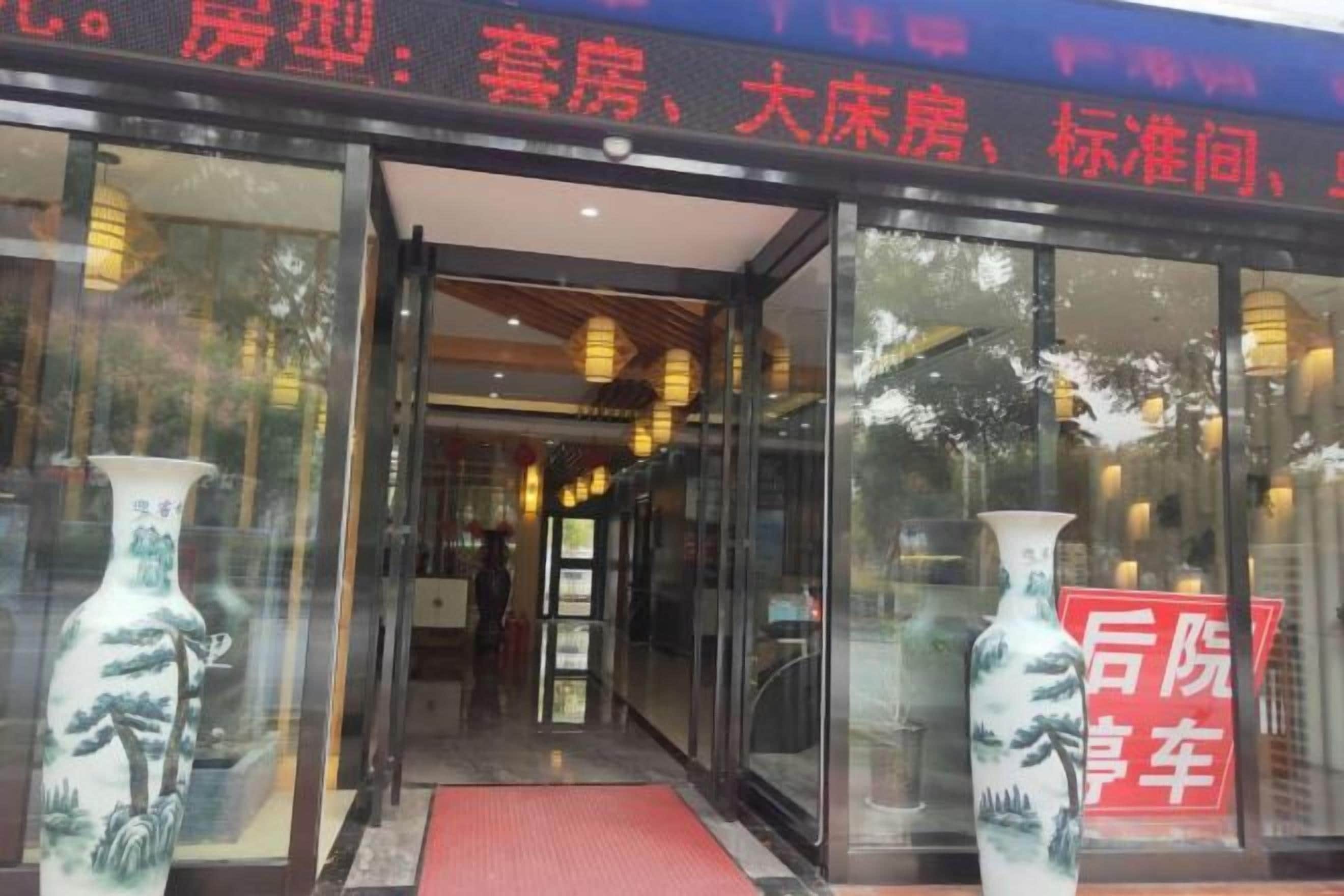 A hotel entrance with glass doors, a red mat, and two vases on either side.