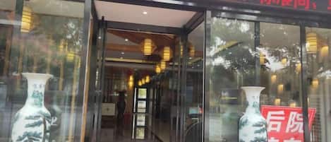 Entrada de un hotel con puertas de vidrio, un felpudo rojo y dos jarrones a cada lado.