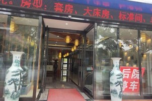 Entrada de un hotel con puertas de vidrio, un felpudo rojo y dos jarrones a cada lado.