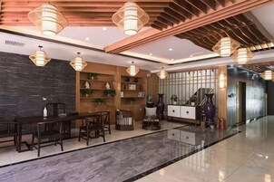 Un moderno vestíbulo de hotel con suelo de mármol, mostrador de recepción de madera e iluminación colgante.