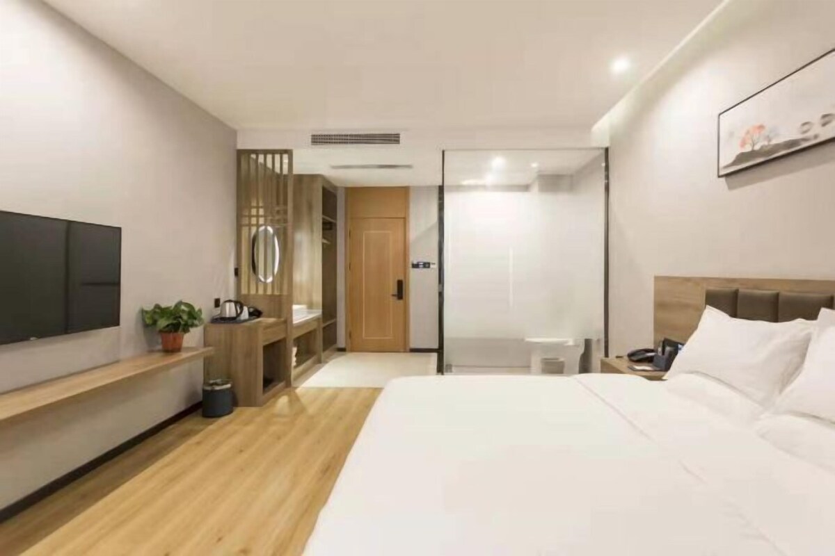 A modern hotel room with a large bed, a TV, a desk, and a wardrobe.