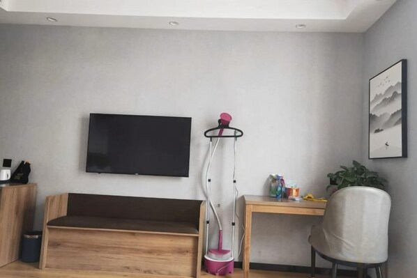 Una sala de estar moderna con una televisión de pantalla plana montada en la pared, un banco de madera, un escritorio con una silla y una lámpara de pie.