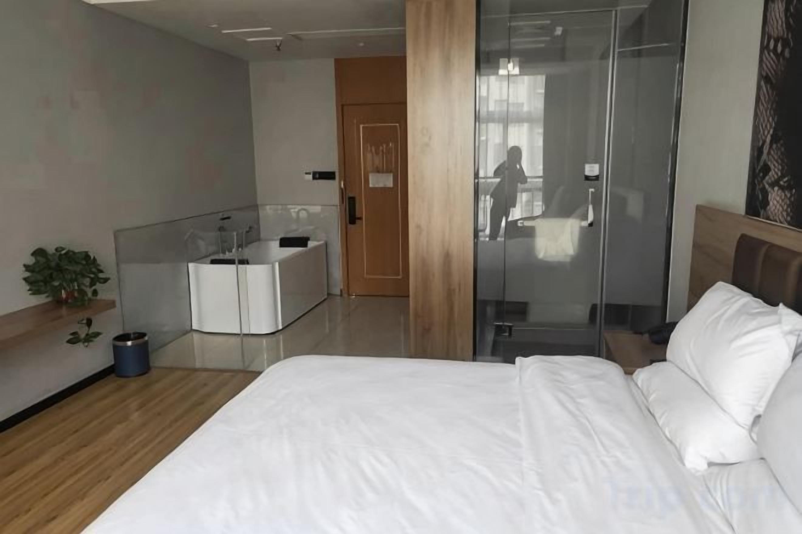 Habitación de hotel moderna con una cama grande, cabina de ducha con vidrio, mesita de noche pequeña y escritorio integrado con espejo.