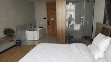 Habitación de hotel moderna con una cama grande, cabina de ducha con vidrio, mesita de noche pequeña y escritorio integrado con espejo.