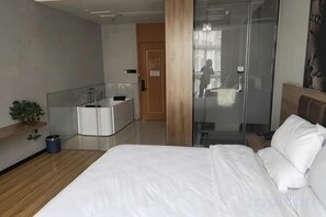 A modern hotel room with a large bed, a glass shower enclosure, a small bedside table, and a built-in desk with a mirror. - Tonghuali Hotel (Lankao)