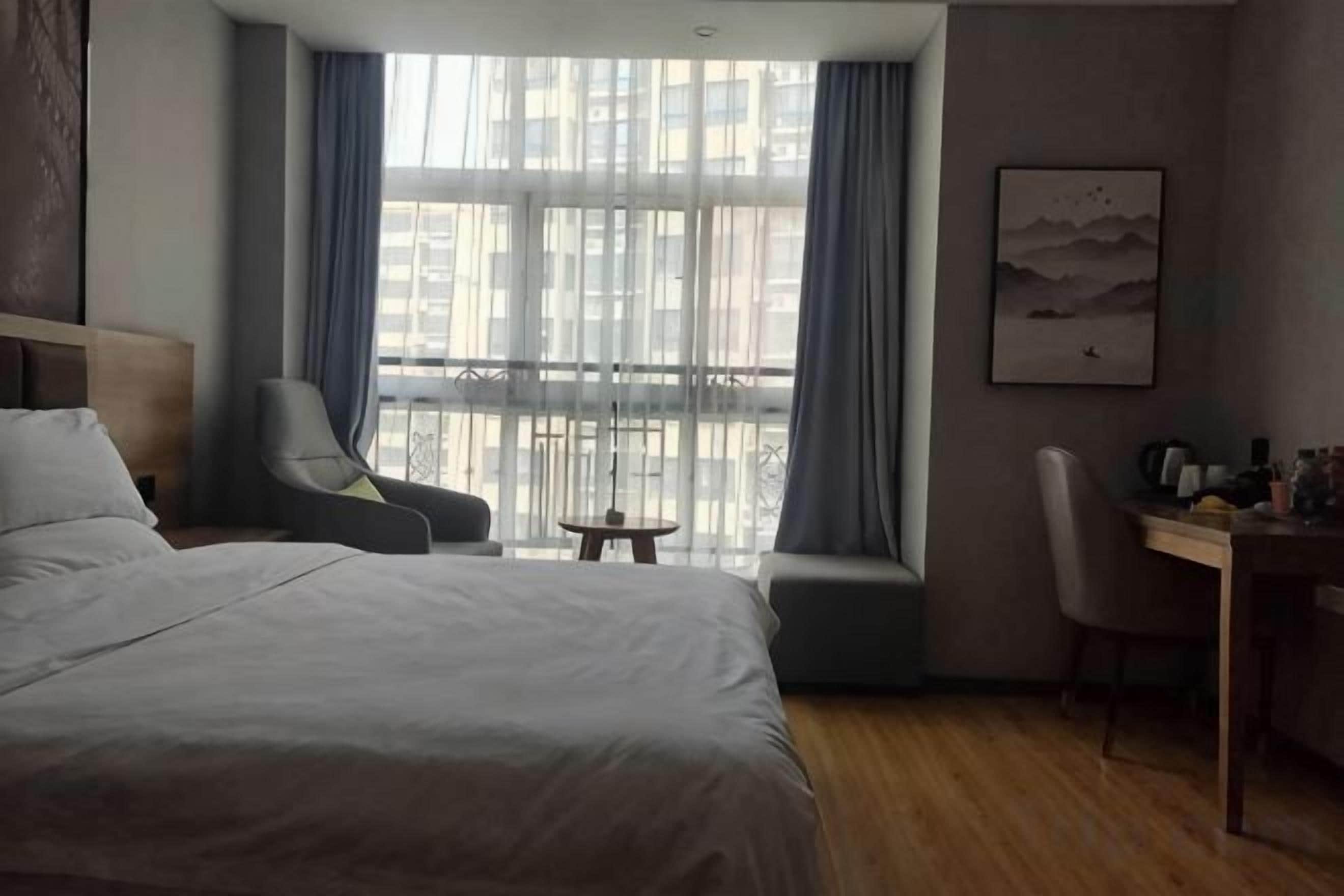Quarto de hotel com cama, cadeira, escrivaninha e janela com cortinas.