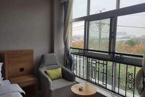 A hotel room with a balcony, a bed, a chair, and a small table. - Tonghuali Hotel (Lankao)
