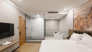Una habitación de hotel moderna con una cama grande, un televisor montado en la pared, una zona de ducha y un cuadro en la pared.
