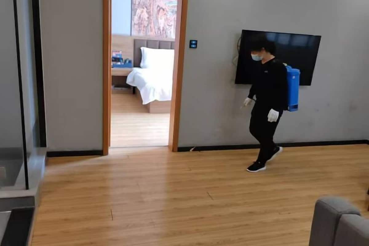 Una habitación de hotel con una cama, un televisor y una persona cargando una maleta azul.