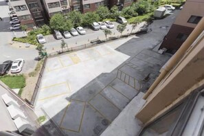 Un estacionamiento con espacios delimitados, un edificio de fachada color crema y una fila de coches aparcados.