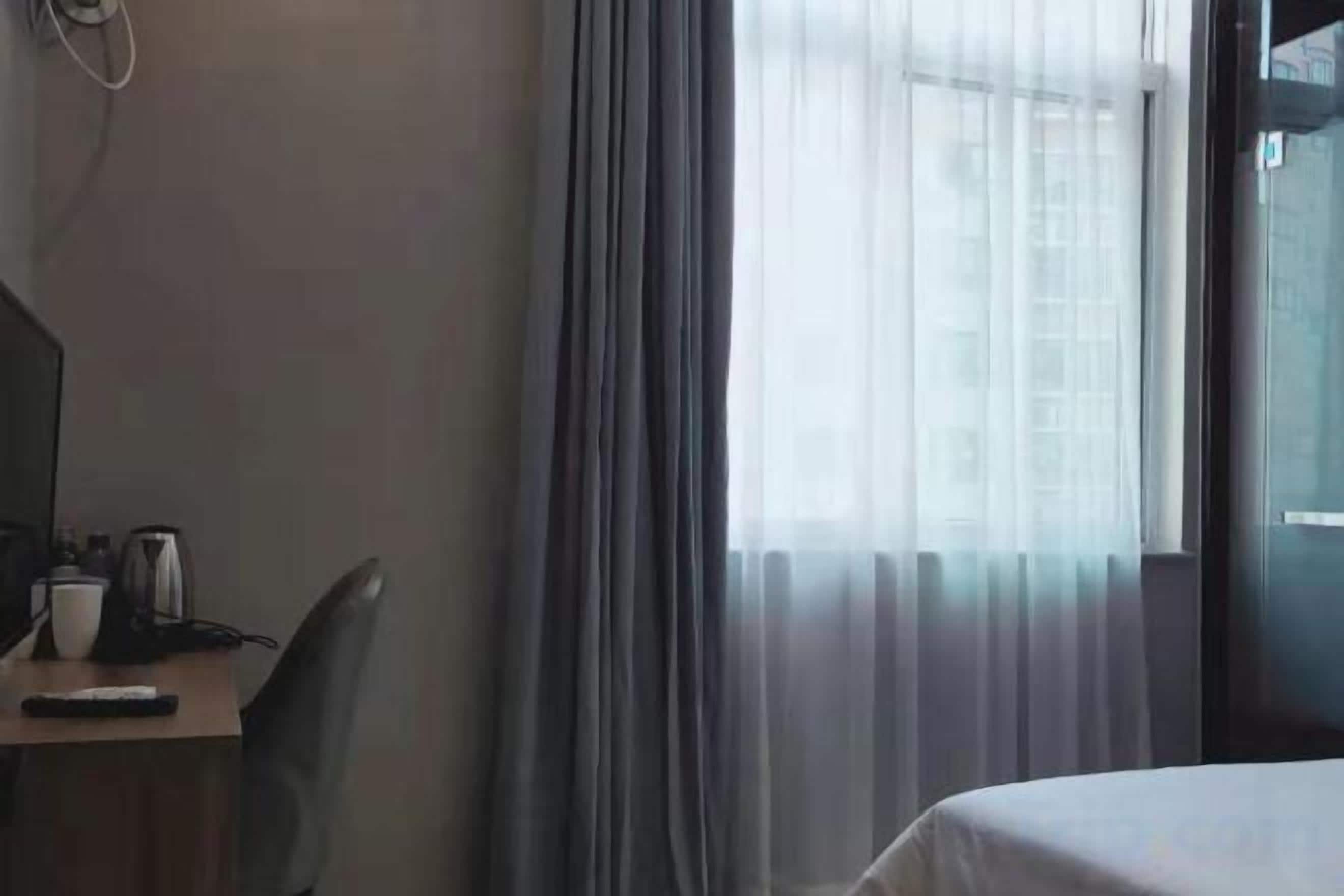 Ein Hotelzimmer mit einem Bett, einem Schreibtisch mit Stuhl, einer Kaffeemaschine und einem Fenster mit Vorhängen.