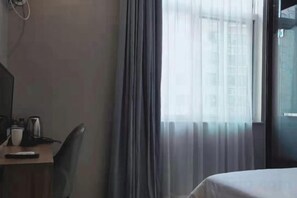 A hotel room with a bed, a desk with a chair, a coffee maker, and a window with curtains. - Tonghuali Hotel (Lankao)