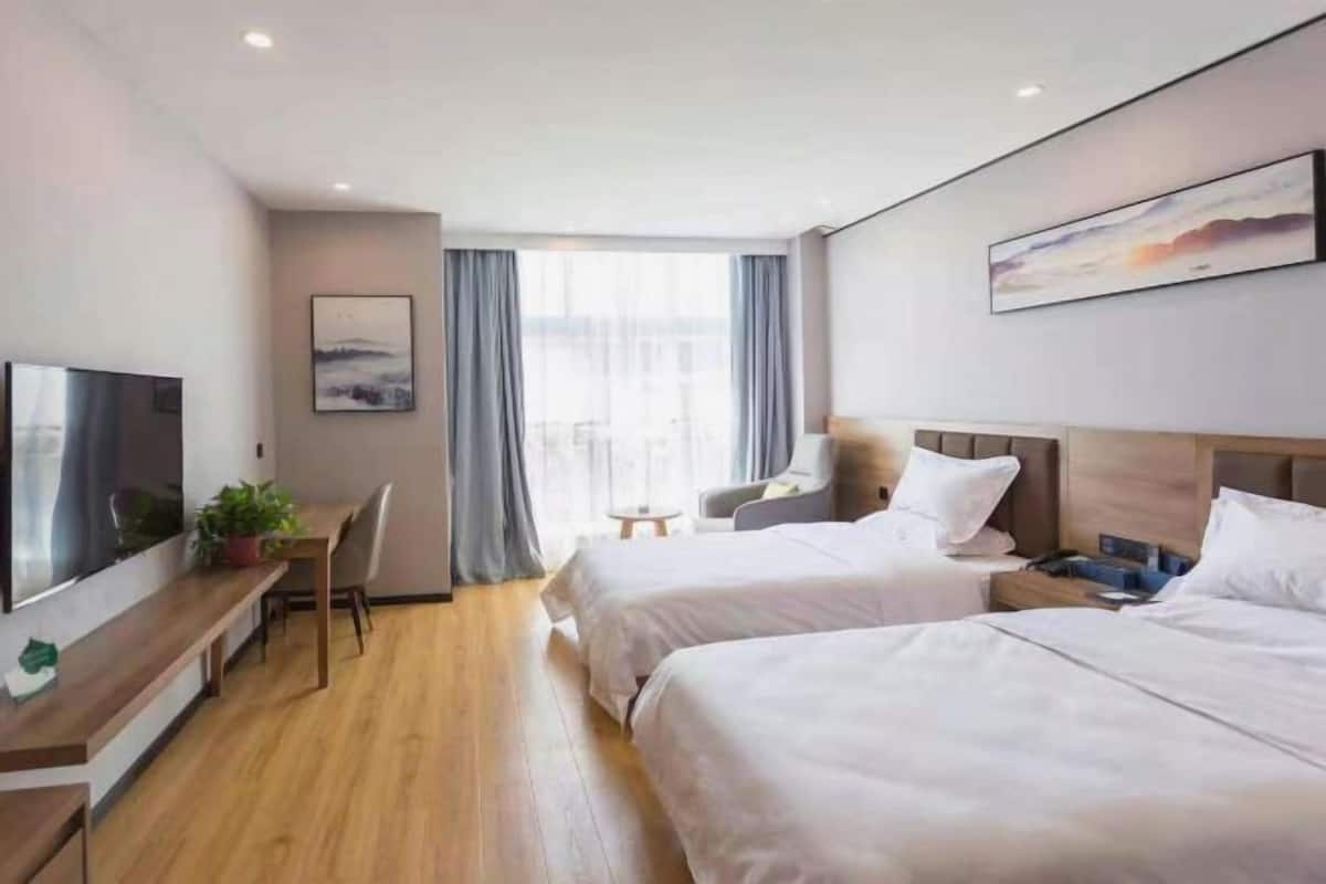 Habitación de hotel con dos camas, un escritorio con silla, televisor y ventana con cortinas.