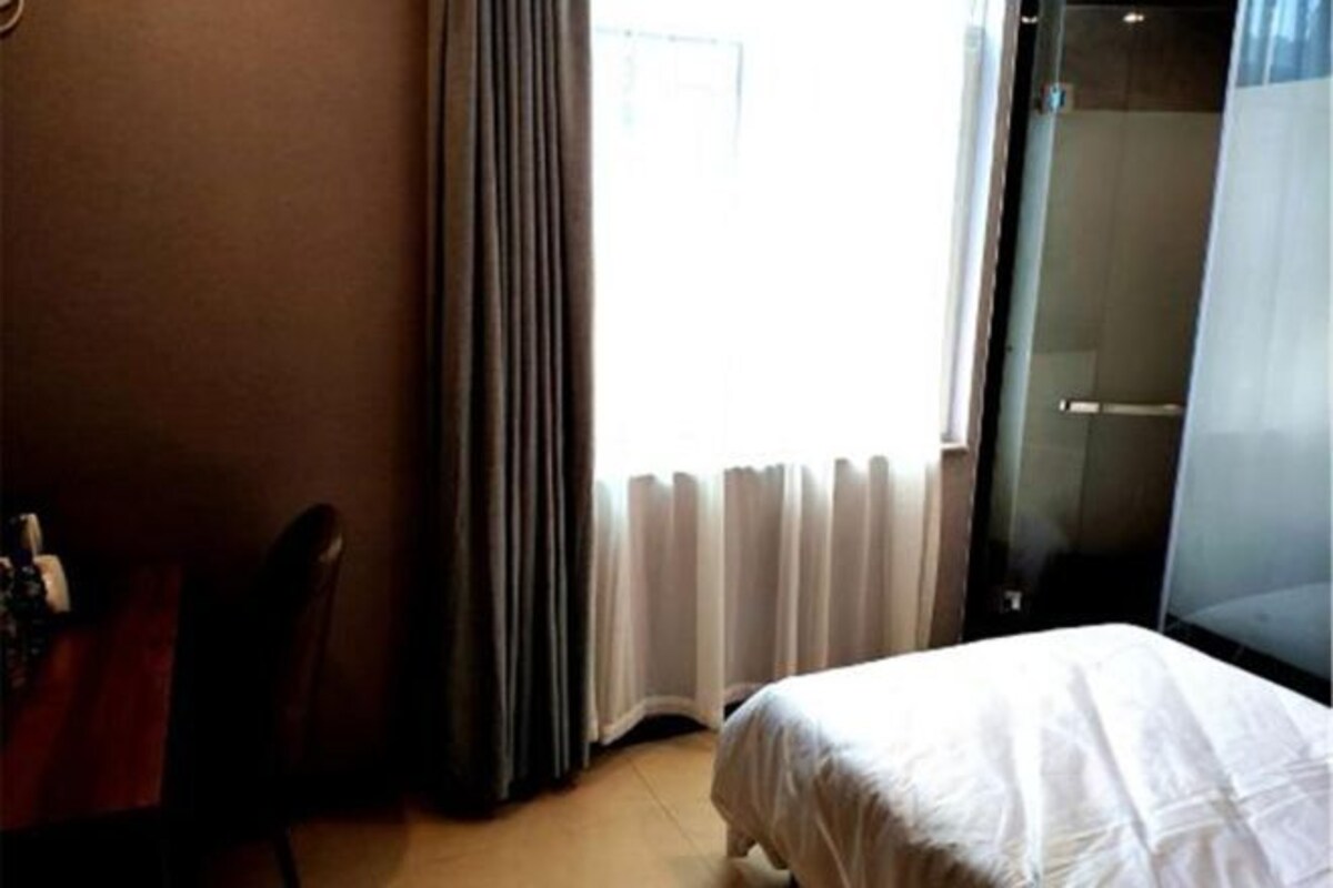 A hotel room with a bed, a chair, a desk, and a window with curtains.