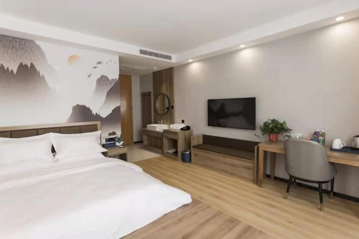 Habitación de hotel con cama, escritorio, silla, televisor, lavabo y espejo.