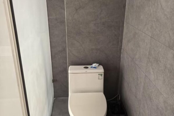 Un baño pequeño y estrecho con inodoro, una puerta blanca y paredes con azulejos grises.