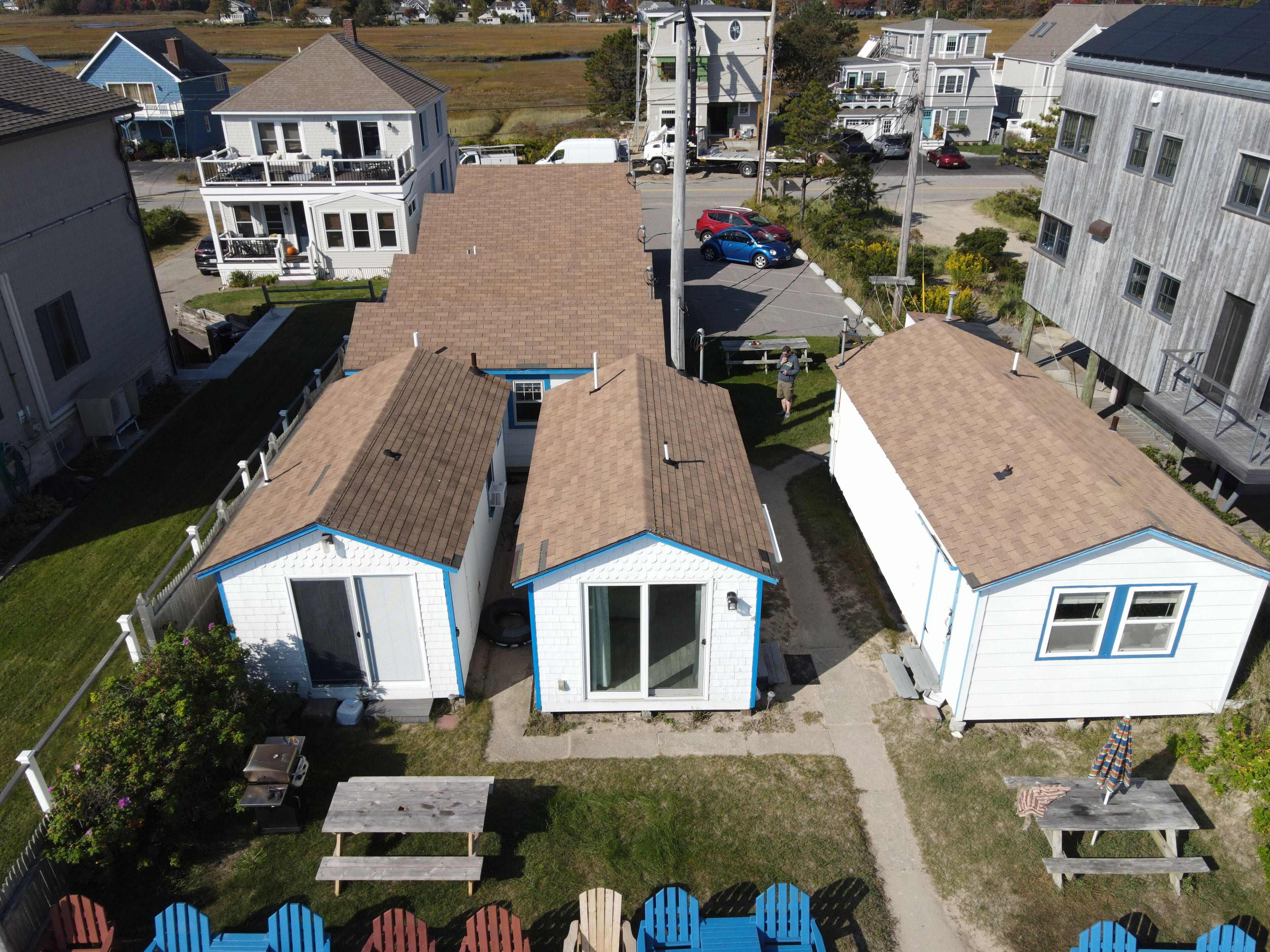 Un barrio residencial con dos pequeñas casas de una sola planta, detalles azules, una mesa de picnic y sillas Adirondack.