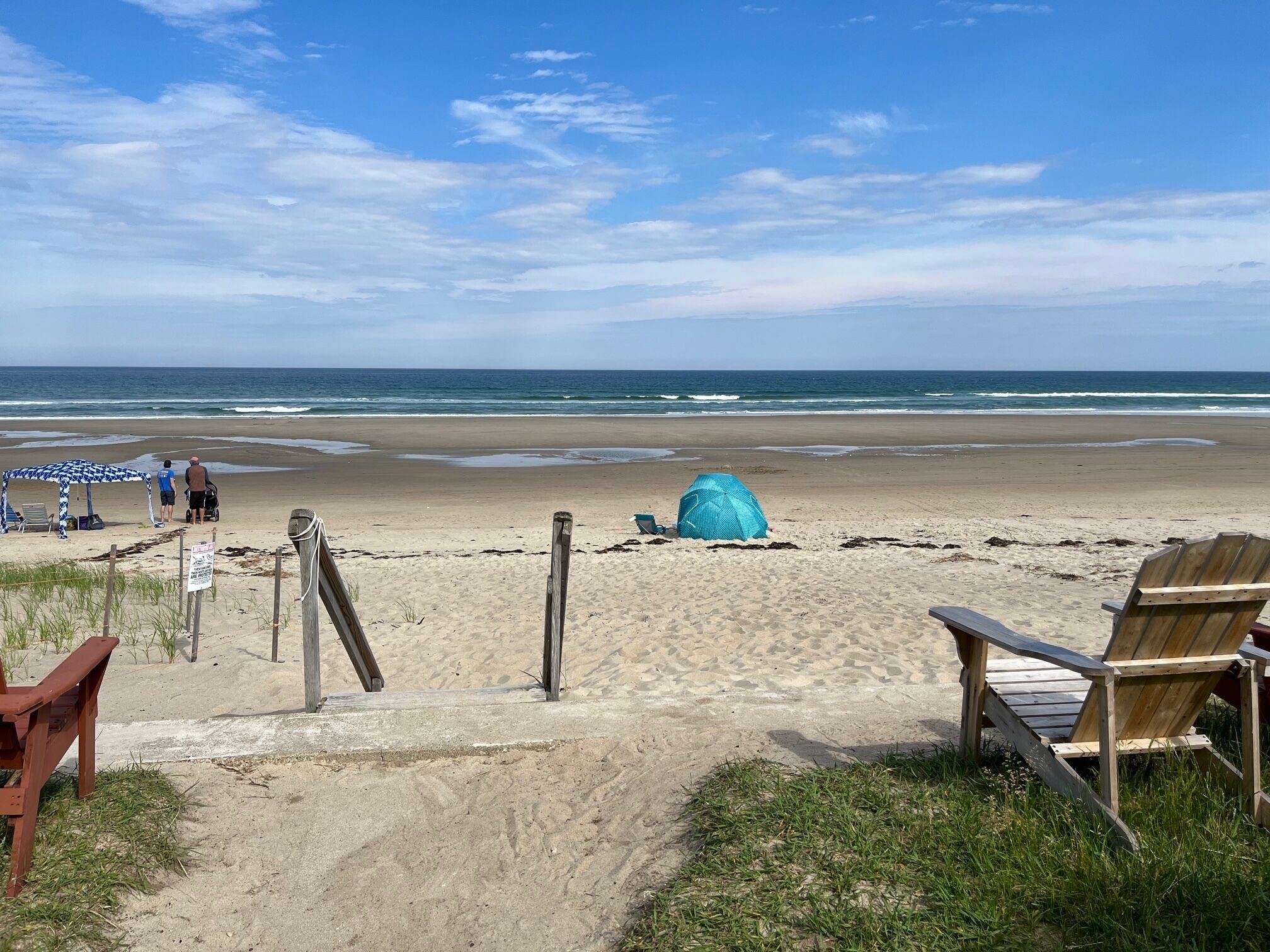 A beach with a wooden deck, a blue tent, and a wooden chair.