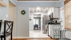 Una cocina moderna con armarios blancos, un refrigerador de acero inoxidable y un comedor con mesa y sillas.
