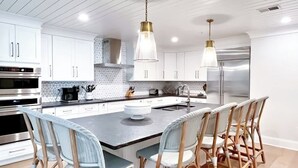 A modern kitchen with white cabinets, stainless steel appliances, a central island with chairs, and pendant lighting.