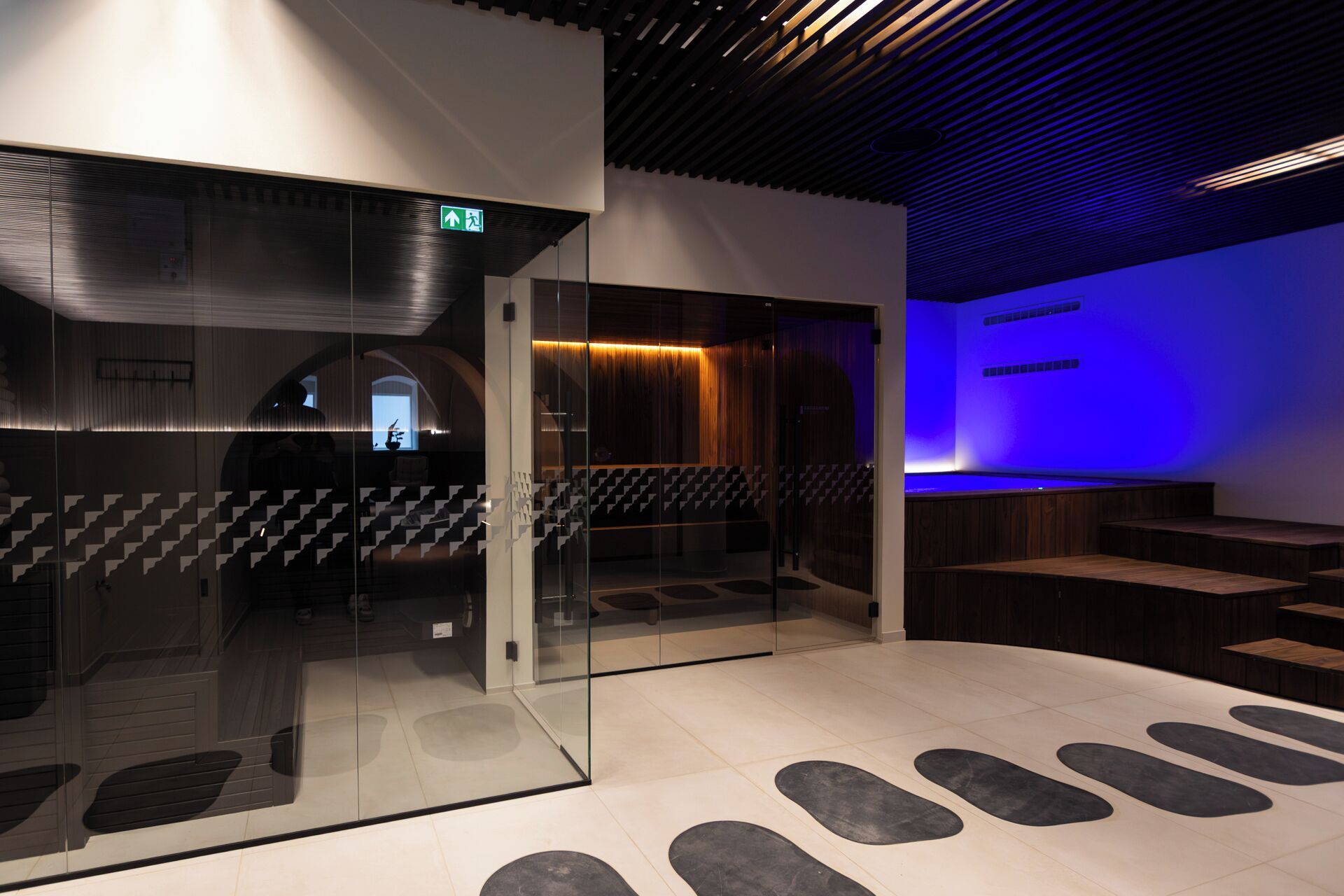 Een modern interieur met een glazen scheiding, een trap en een zithoek met een blauw verlichte wand.