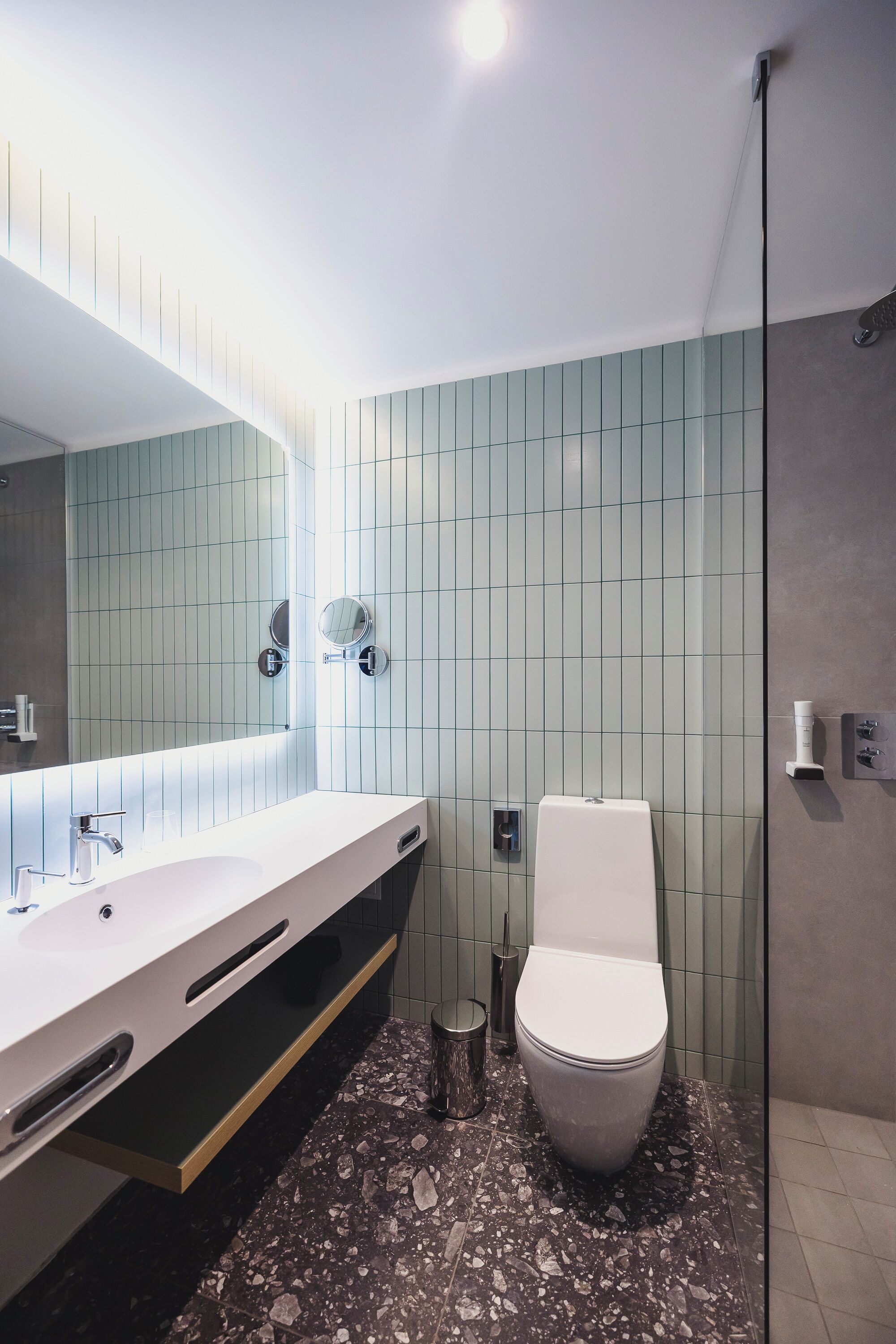 A modern bathroom with a large mirror, a white sink, and a toilet.