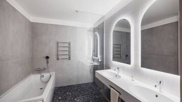 Un baño moderno con bañera, dos lavamanos y un espejo grande.