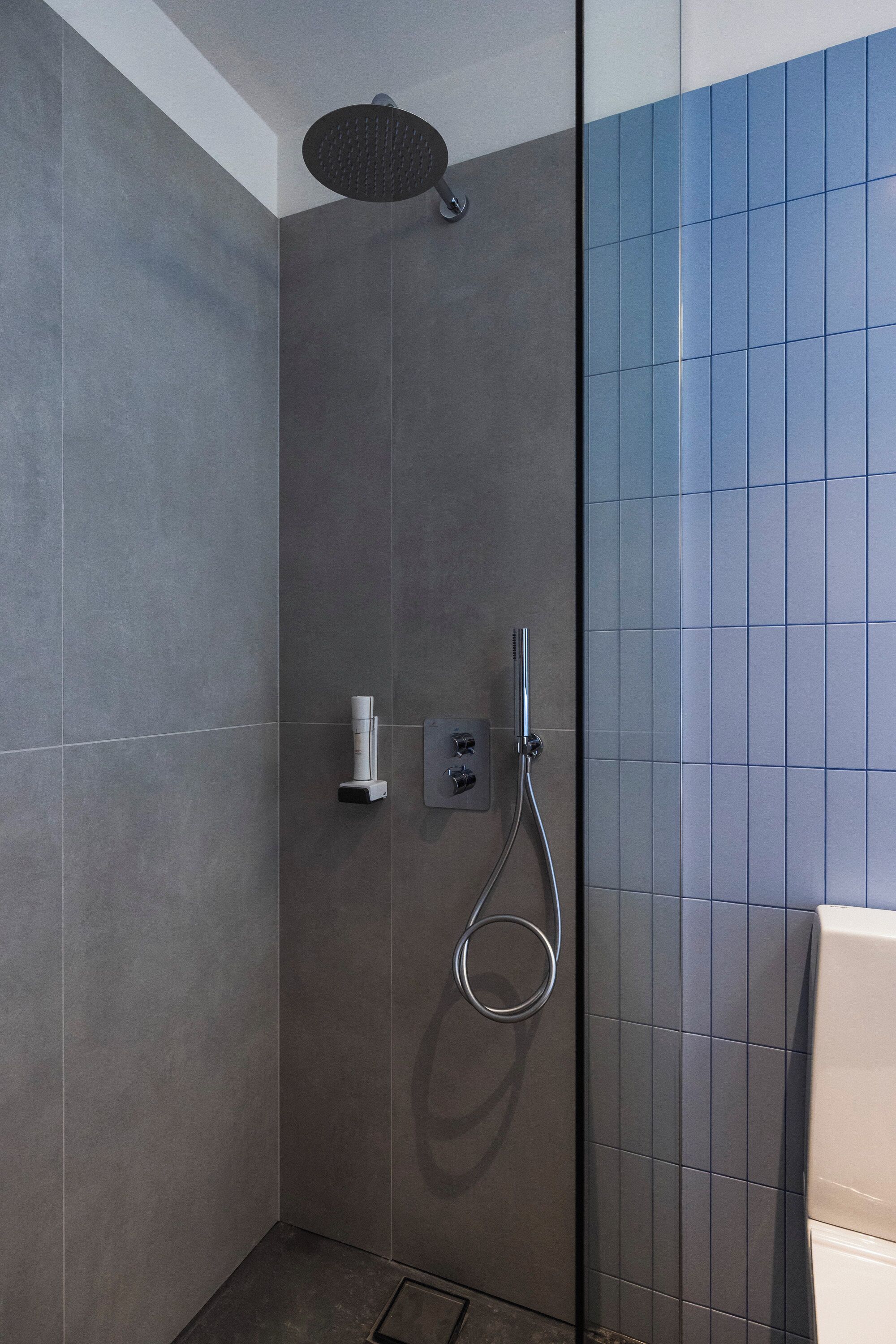 A shower area with a handheld showerhead, a wall-mounted control panel, and a glass partition.