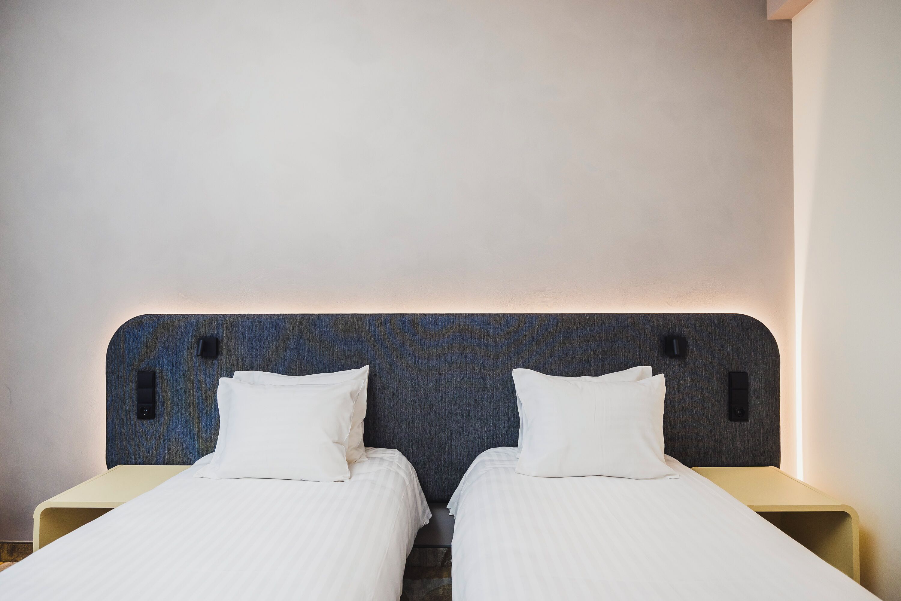 A double bed with a textured headboard, two bedside tables, and a wall-mounted light.
