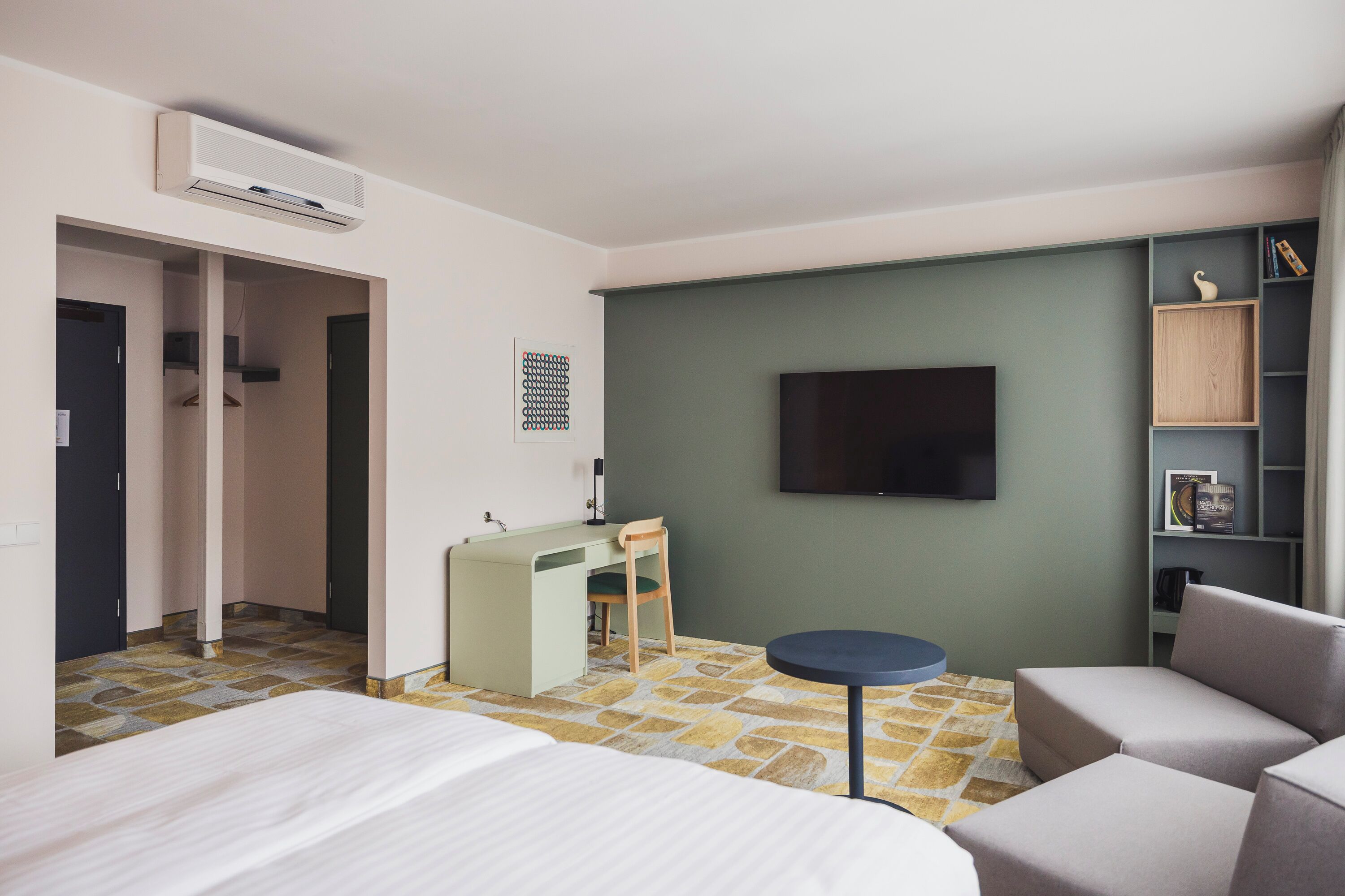 Habitació d'hotel amb un llit, escriptori, cadira, televisió i prestatgeria.