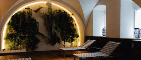 Un interior con piso de madera curvada, dos sillones de descanso y una pared con jardín vertical iluminado por luces LED.
