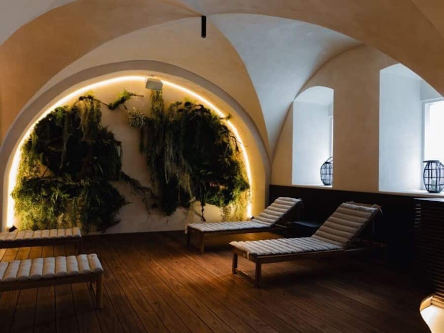 Un interior amb un sòl de fusta corbat, dues butaques relaxants i una paret amb un jardí vertical verd il·luminat per llums laterals.
